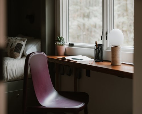 A tidy workspace by the window with a wooden laptop stand and a notebook reflecting a balanced remote work setup