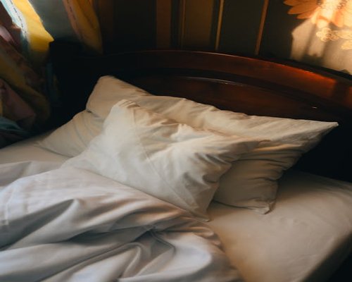 A dimly lit cozy bedroom with a wooden bedframe and white cotton sheets emphasizing a healthy sleeping environment